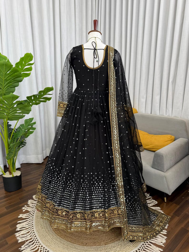 Peut inclure: Longue robe noire avec des manches longues et transparentes et un col rond. La robe est orn&eacute;e de paillettes argent&eacute;es et de broderies dor&eacute;es le long de l'ourlet et des poignets. Une &eacute;charpe transparente noire assortie avec une bordure dor&eacute;e.