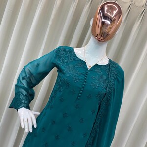 May include: A teal long-sleeved tunic featuring intricate tonal floral embroidery on the bodice and cuffs. The garment has a round neckline with a vertical row of matching fabric buttons down the center front and includes a coordinating sheer shawl.