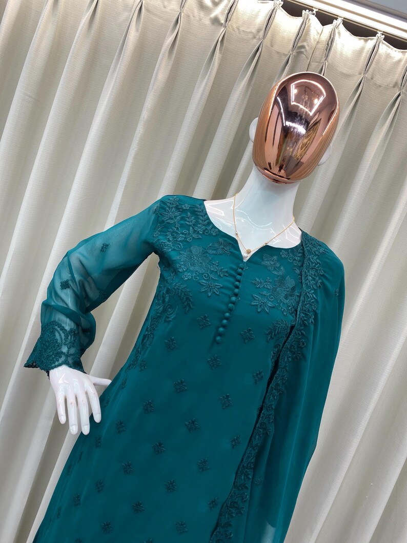 May include: A teal long-sleeved tunic featuring intricate tonal floral embroidery on the bodice and cuffs. The garment has a round neckline with a vertical row of matching fabric buttons down the center front and includes a coordinating sheer shawl.