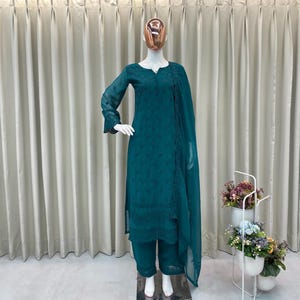 May include: A teal long-sleeved tunic with intricate tonal embroidery, paired with matching straight-leg trousers and a coordinating sheer dupatta. The ensemble features a round neckline with a button placket and delicate scalloped hem details.