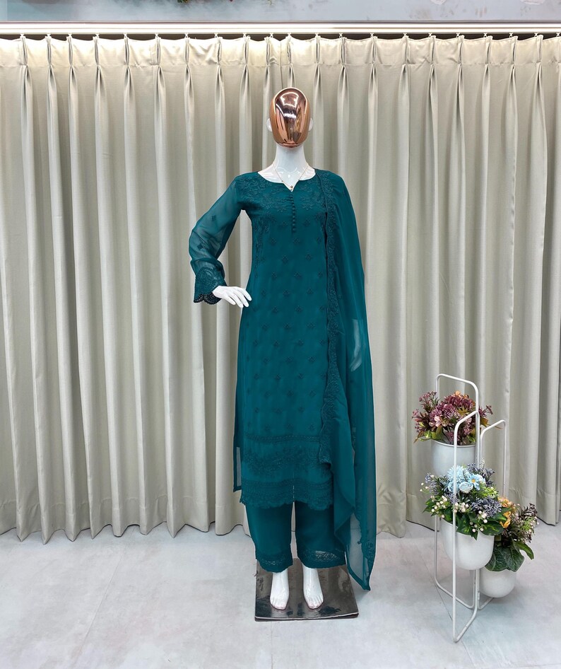 May include: A teal long-sleeved tunic with intricate tonal embroidery, paired with matching straight-leg trousers and a coordinating sheer dupatta. The ensemble features a round neckline with a button placket and delicate scalloped hem details.
