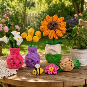 May include: A collection of crocheted items including a pink vase with white calla lilies, a purple vase with yellow flowers, a large sunflower in a green and white pot, a small bee, a pink flower, and a tan vegetable with green leaves.