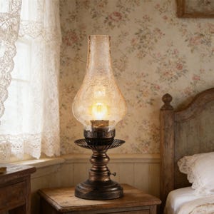 May include: An antique-style table lamp with a textured amber glass shade and a bronze-colored metal base. The lamp is lit, casting a warm glow. The lamp is sitting on a wooden nightstand.