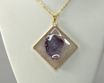 May include: A gold chain necklace with a square pendant featuring a purple and white agate stone.