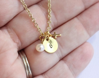 May include: A gold chain necklace with a small gold cross charm, a pearl charm, and a gold disc charm with the letter "B" engraved on it.