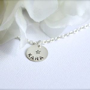 May include: A silver necklace with a round pendant that says "KARA" with a small star above the name.