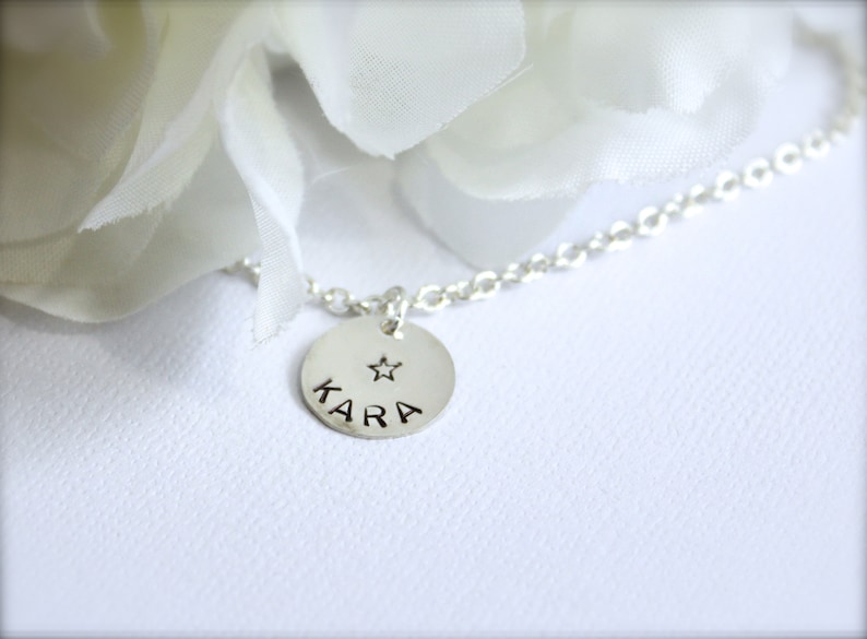May include: A silver necklace with a round pendant that says "KARA" with a small star above the name.