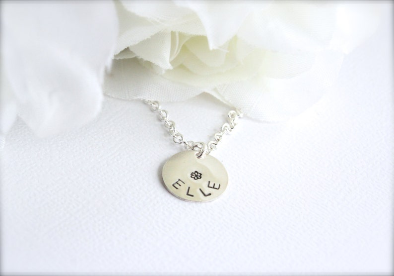 May include: A silver necklace with a round pendant that says "ELLE" with a small flower design in the center.