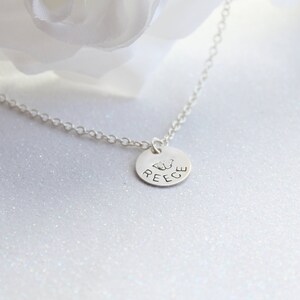 May include: Silver necklace with a round pendant featuring the name "REECE" and a butterfly design.