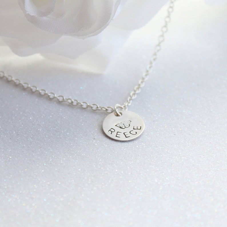 May include: Silver necklace with a round pendant featuring the name "REECE" and a butterfly design.