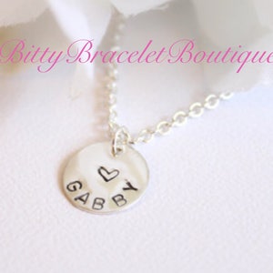 May include: Silver necklace with a round charm that says "GABBY" with a small heart above the Y.