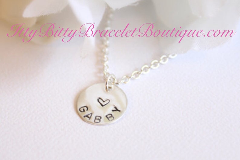 May include: Silver necklace with a round charm that says "GABBY" with a small heart above the Y.