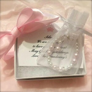Puede incluir: Una caja de regalo blanca con una cinta rosa y una bolsa de organza blanca que contiene un brazalete de perlas. La caja tiene una tarjeta en el interior que dice "Sele We are to have you May God bless you always. Love The Faadaway's".