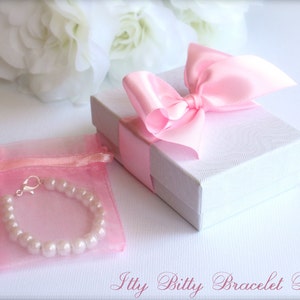 May include: A pink pearl bracelet in a pink organza bag with a silver clasp. The bracelet is packaged in a white gift box with a pink satin bow.