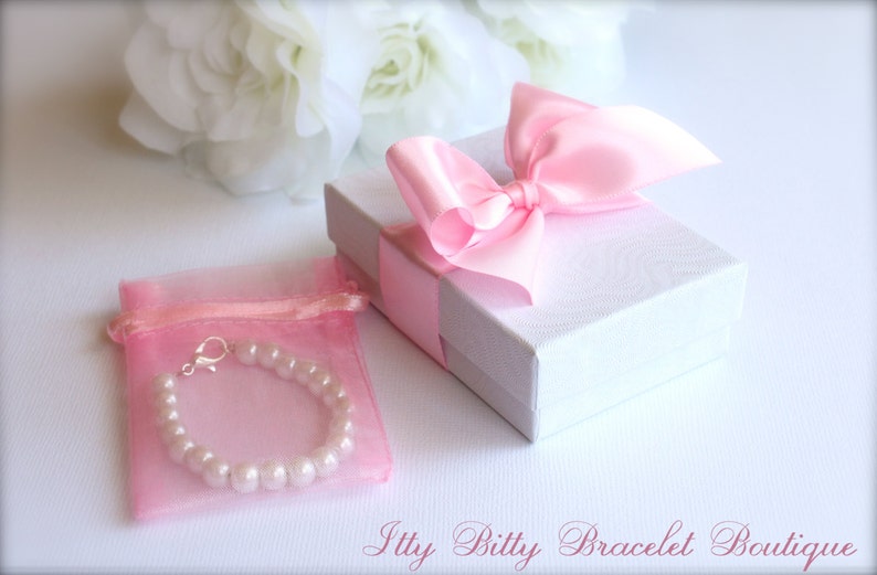 May include: A pink pearl bracelet in a pink organza bag with a silver clasp. The bracelet is packaged in a white gift box with a pink satin bow.
