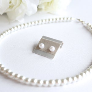 Puede incluir: Un conjunto de pendientes de perlas y un collar de perlas. Los pendientes est&aacute;n en una peque&ntilde;a tarjeta de exhibici&oacute;n. El collar est&aacute; hecho de perlas blancas y est&aacute; dispuesto en c&iacute;rculo.