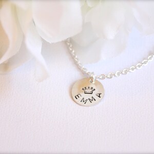 May include: A silver necklace with a round pendant that says "EMMA" with a small crown above the name.