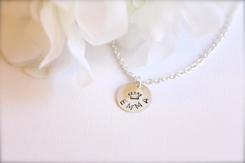 May include: A silver necklace with a round pendant that says "EMMA" with a small crown above the name.