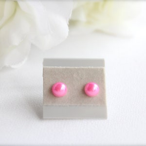 May include: A pair of pink pearl stud earrings on a white display card.