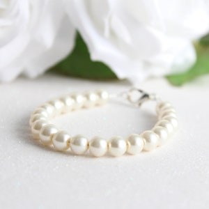 May include: A white pearl bracelet with a silver clasp. The bracelet is on a white background.