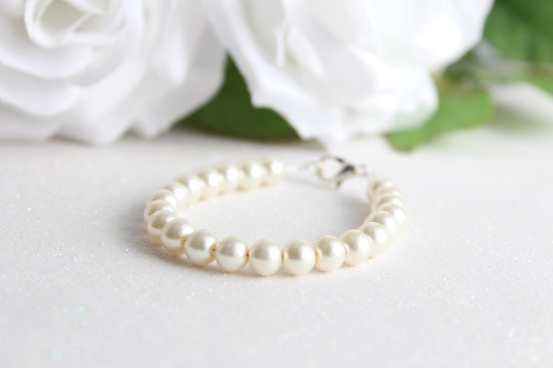 May include: A white pearl bracelet with a silver clasp. The bracelet is on a white background.