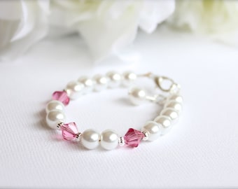 May include: A white pearl bracelet with pink crystal accents and a matching pair of earrings. The bracelet has a silver clasp.
