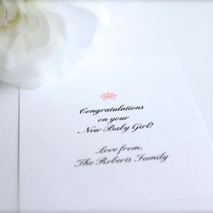 May include: A white card with black text that reads "Congratulations on your New Baby Girl! Love from, The Roberts Family". A pink crown is above the text.