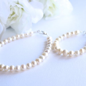 May include: A set of two pearl necklaces, one longer than the other, both with a silver clasp. The necklaces are on a white surface.
