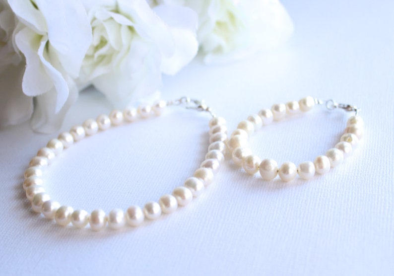 May include: A set of two pearl necklaces, one longer than the other, both with a silver clasp. The necklaces are on a white surface.