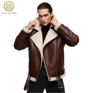 May include: A brown leather jacket with a cream-colored shearling lining and collar. The jacket features a zip closure, a buckled belt, and a logo in the upper left corner. The jacket is a classic style.