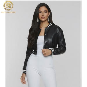 May include: Black cropped leather jacket with white stripes on the cuffs and collar. The jacket has a button-up front and is worn over a white top and white pants. The jacket is from Elite Leather.