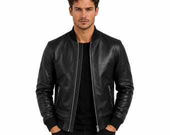 May include: A black leather bomber jacket featuring a ribbed collar, cuffs, and hem. The jacket has a central silver-toned metal zipper closure and two side pockets with silver-toned zippers, worn over a plain black shirt and black pants.
