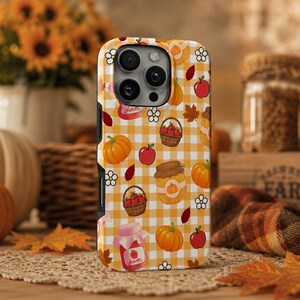 Peut inclure: Une coque de smartphone avec un motif vichy jaune et blanc orné d'illustrations de citrouilles, de pommes rouges, de paniers de fruits, de pots de confiture et de petites fleurs blanches. Le motif couvre tout le dos de la coque.
