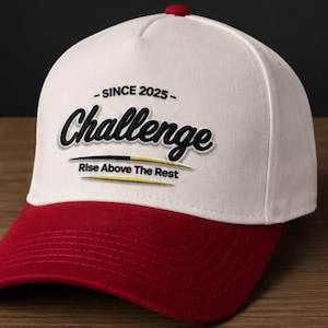 Könnte beinhalten: Eine weiß-rote Baseballkappe mit dem Wort "Challenge" in schwarzer Schrift. Die Kappe hat außerdem den Text "- SINCE 2025 -" und "Rise Above The Rest". Die Kappe hat einen roten Schirm und einen roten Knopf oben.