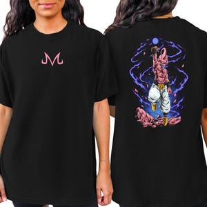 May include: Black t-shirt featuring a pink "M" logo on the front. The back of the shirt displays a colorful illustration of a character with a blue energy ball, surrounded by purple energy lines and pink rocks.