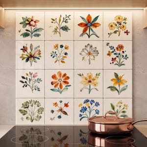 May include: A square backsplash composed of sixteen white ceramic tiles, each featuring a unique watercolor-style botanical illustration of various flowers and foliage in shades of orange, yellow, blue, and green, installed above a black stovetop.