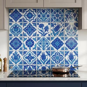 Può includere: Un paraschizzi da cucina con un motivo ripetuto di piastrelle floreali blu e bianche. Le piastrelle sono disposte a griglia, creando un elemento decorativo e funzionale. Una padella color rame è su un piano cottura nero.