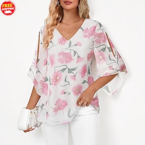 Peut inclure: Chemisier blanc à col en V et manches fendues, orné d'un motif floral rose et de feuilles vertes. Le haut a un design fluide et léger, parfait pour un look décontracté ou semi-formel.