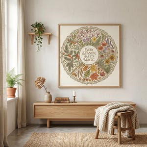 May include: A framed print featuring the text "Every Season Has Its Magic" within a circular botanical design. The artwork showcases illustrations of the four seasons in green, brown, yellow, and red hues. The frame is made of light-colored wood.