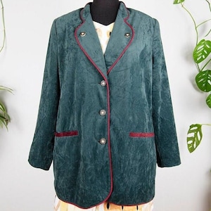 Puede incluir: Una chaqueta de terciopelo verde oscuro con ribete de terciopelo rojo. La chaqueta tiene cierre de botones y dos bolsillos.