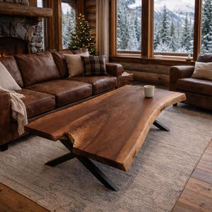 May include: A rustic living room features a large, live-edge wooden coffee table with black metal legs. The table sits on a gray rug in front of a brown leather sectional sofa. A fireplace and large windows offer a view of a snowy mountain.