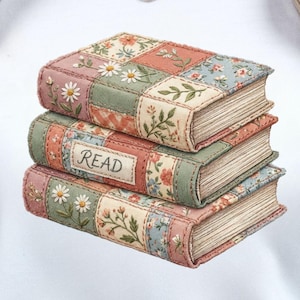 Op de afbeelding: Wit T-shirt met een afbeelding van drie gestapelde boeken. De boeken hebben bloemen- en patchworkpatronen in roze, groen en blauw. Het middelste boek heeft het woord "READ" erop. De boeken zijn op elkaar gestapeld.