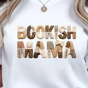 Può includere: T-shirt bianco con la scritta "BOOKISH MAMA" in un carattere decorativo e strutturato. Le lettere presentano vari motivi, tra cui stampa leopardata, disegni floreali e trame a maglia. La maglietta è di stile casual.