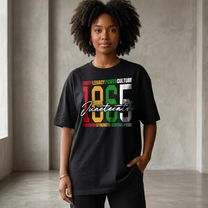 K&ouml;nnte beinhalten: Schwarzes T-Shirt mit dem Wort "Juneteenth" in Schreibschrift und den Zahlen "1865" in fetter, farbiger Schrift. Das Shirt zeigt auch die W&ouml;rter "Unity Legacy Power Culture" und "Freedom Strength Heritage Pride".