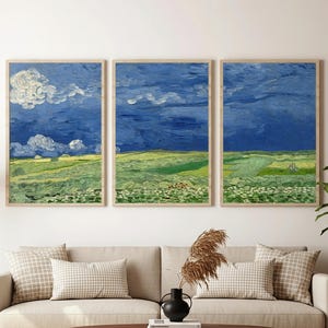 May include: A set of three framed landscape paintings in the style of Van Gogh. The artwork depicts a dramatic blue sky with white clouds over a green and yellow field. The frames are a light wood colour, complementing the artwork's colours.