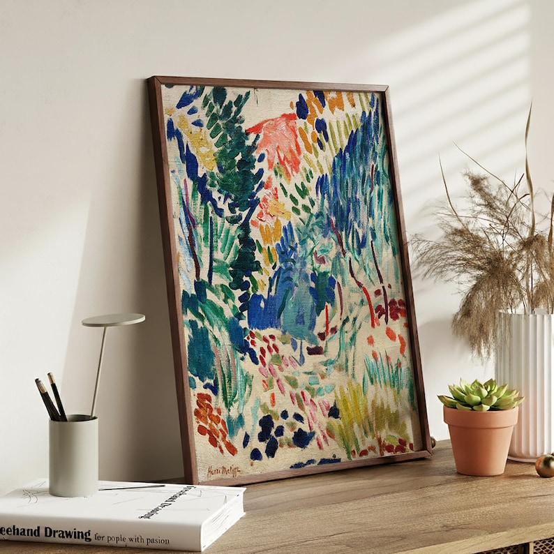 May include: A framed abstract painting with a brown wooden frame. The artwork features a colorful landscape with blue, green, red, and yellow brushstrokes. The painting is leaning against a white wall, with a small succulent in a terracotta pot.