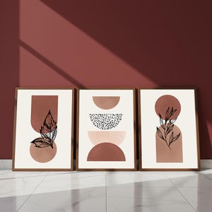 Peut inclure: Trois impressions d'art encadrées avec des motifs botaniques abstraits. Chaque impression présente une palette de couleurs neutres avec des formes géométriques, dont des cercles et des arches, et des illustrations de feuilles détaillées. Les cadres sont de couleur marron chaud.