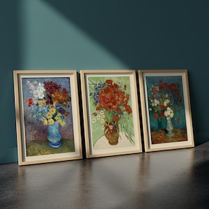May include: Three framed art prints featuring floral still life paintings. The artworks showcase bouquets of colorful flowers in vases, with a focus on vibrant reds, blues, and yellows. The frames are light-colored wood.