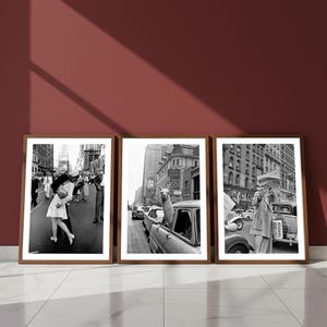 May include: Three framed black and white photographs. The images depict scenes from a city street, including a couple kissing, a llama in a car, and a person reading a newspaper. The frames are brown and the background is a dark red.