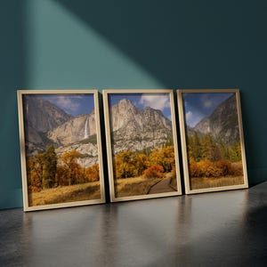 May include: Three framed landscape prints depicting mountain scenery with waterfalls, trees, and a wooden walkway. The frames are a light beige colour, and the artwork features autumn colours with blue skies.